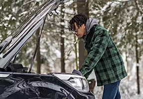 Man standing next to the car with opened hood in the winter scenery